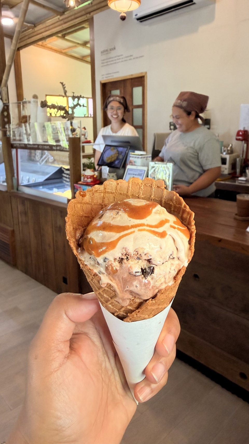 A waffle cone held up at the counter, with two of the shop's people smiling behind it