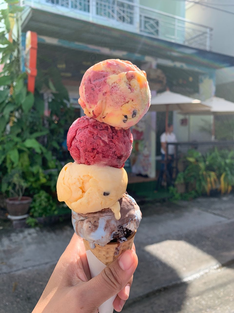 A cone of ice cream with berry sauce, held up against a plain wall