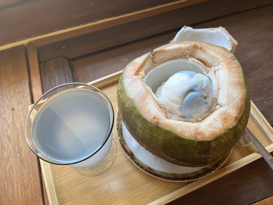 A scoop of ice cream served inside a whole young coconut, with a glass of coconut water beside it