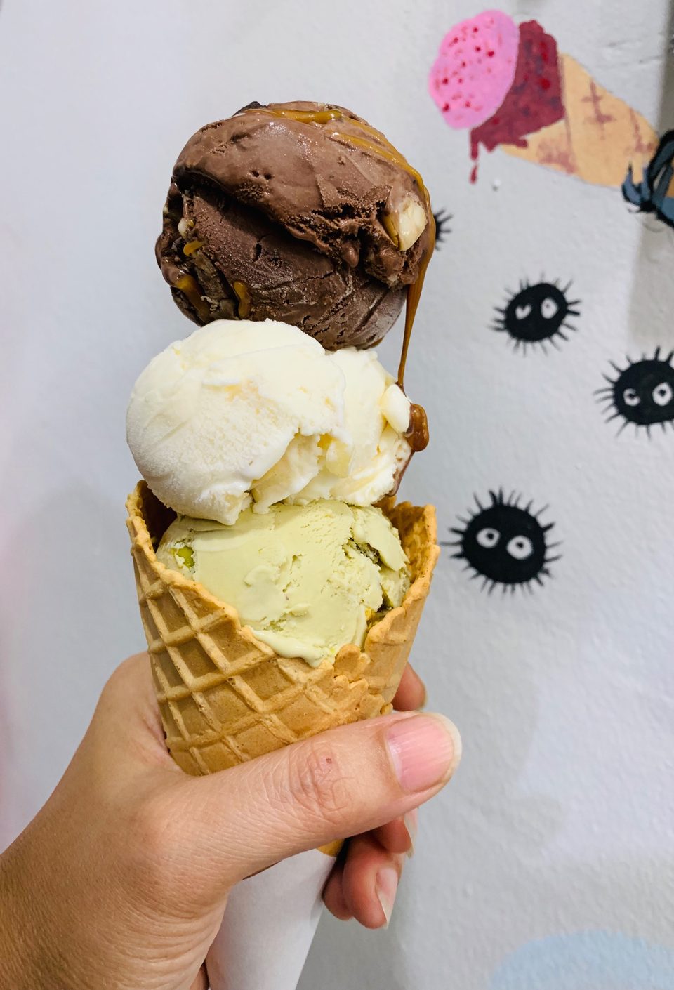 A cone of pale ice cream studded with cookie pieces, held up inside the shop