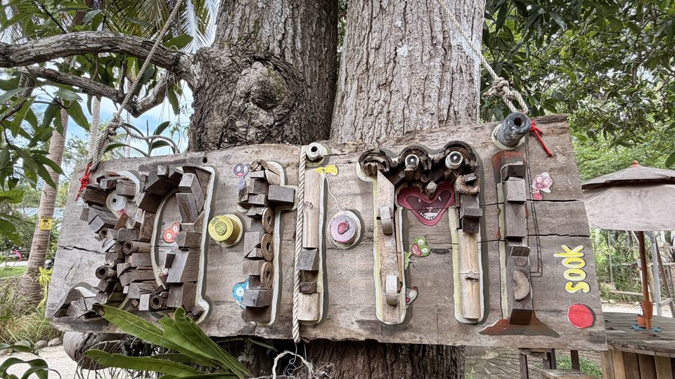 The shop's name spelled out on driftwood with found objects and a carved face, hung on a tree